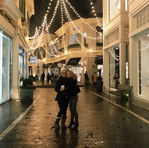 Maya and a friend smiling by holiday lights
