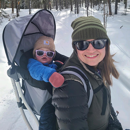 Photo of Kelsey outside in winter with her child in a backpack