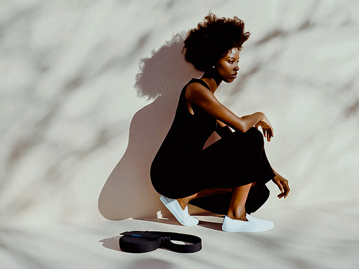 A black woman in a black dress and white shoes leaning against a wall